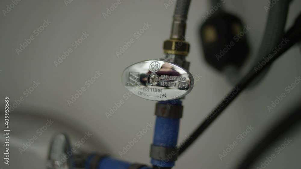 Hand turn off blue cold water valve under sink in kitchen Hand turn off blue cold water valve under sink in kitchen