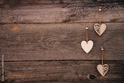 Valentine's Day background. Brown natural boards in grunge style with three wooden decorative hearts. Copy space. Top view. Surface of table to shoot flat lay. Concept love, romantic relation.