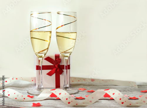 two golden glasses of champagne with a gift box and a red hearts ribbon