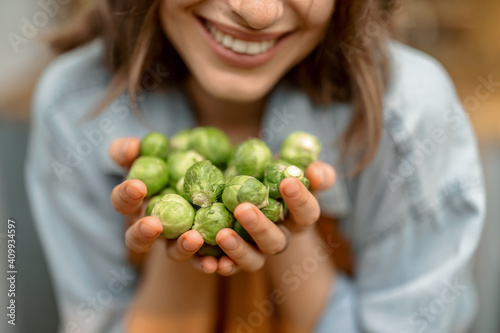 Portrait of pretty woman in apron with fresh brussels sprouts on the kitchen at home. Close up. Healthy cooking concept. High quality photo