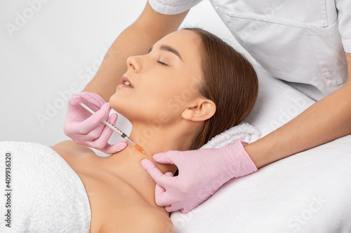 The beautician makes rejuvenating anti wrinkle injections on the face and neck of a beautiful woman. Women's cosmetology in a beauty salon.