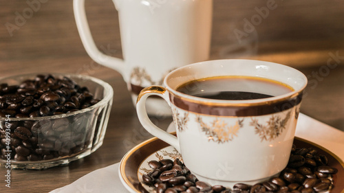 Cup of coffee with smoke and coffee beans on white paper on old wooden background