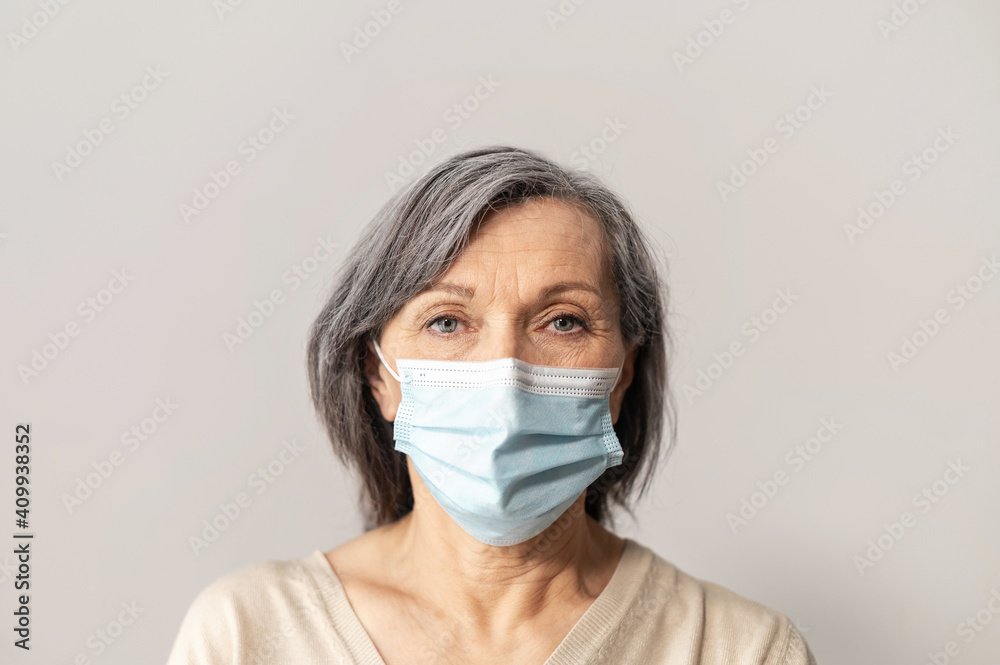 A portrait of senior grey-haired woman wearing protective face mask and looking at the camera intently. Concept of safety and social distance during coronavirus pandemic A portrait of senior grey-haired woman wearing protective face mask and looking at the camera intently. Concept of safety and social distance during coronavirus pandemic
