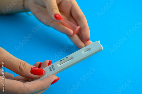 a girl with a bright red manicure holds a coronavirus test and a lancet for a blood test in her hand. determination of IgG and IgM class antibodies. a drop of blood for a test