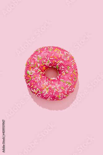 Donut in pink glaze with colorful sprinkles on a pink background
