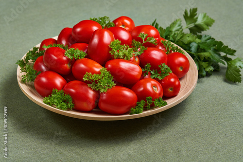 Whole small tomatoes with parsley in a wooden plate is on a green napkin