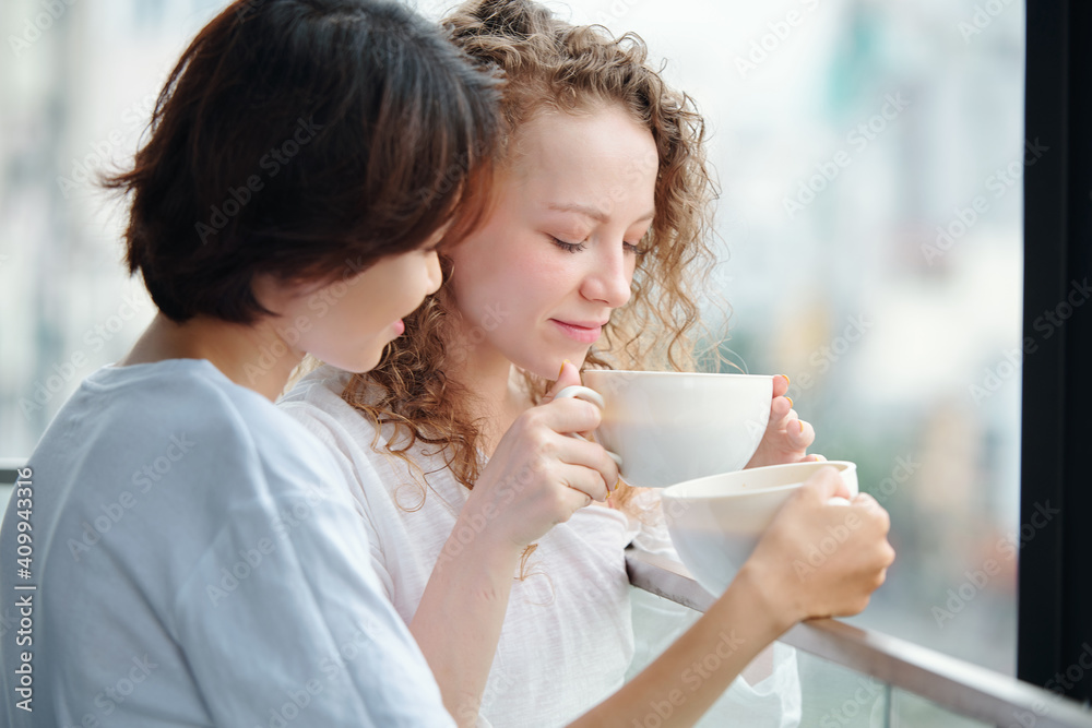 Beautiful young women in love drinking morning coffee on balcony Beautiful young women in love drinking morning coffee on balcony