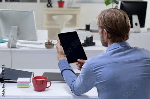 Rear view of caucasian businessman sitting at desk making video call using tabet photo