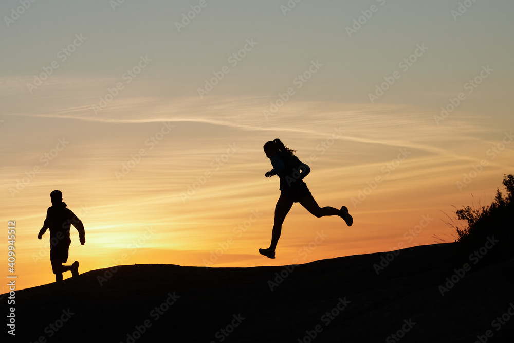 Side view of silhouettes of unrecognizable runners training in rocky terrain in highlands at sundown in summer Side view of silhouettes of unrecognizable runners training in rocky terrain in highlands at sundown in summer
