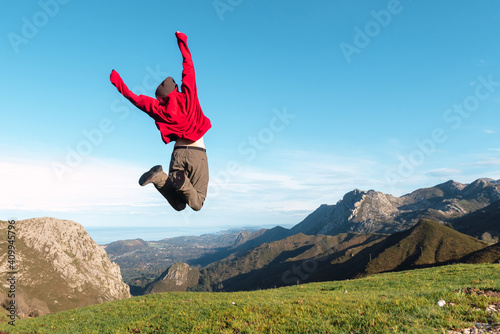 Back view of excited hiker jumping above ground in highlands and enjoying summer vacation in El Mazuco photo