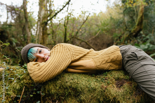 Side view of female explorer lying on tree trunk and having break during trekking in mossy forest