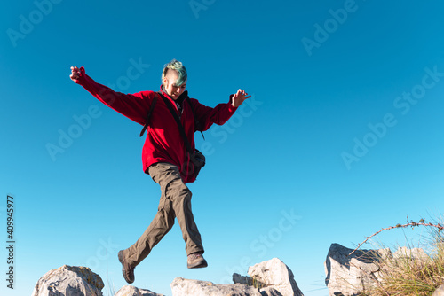 Low angle of energetic hiker jumping on rocks while trekking in highland terrain against blue sky in El Mazuco photo