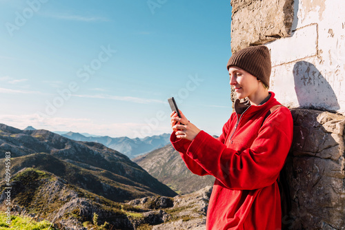 Side view of content hiker standing in highland area and browsing mobile phone while enjoying trekking in El Mazuco on sunny day photo
