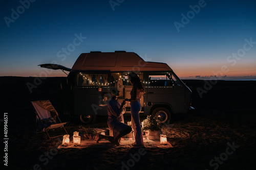 Side view of unrecognizable man making proposal for loving woman while standing on knee near illuminated van at night