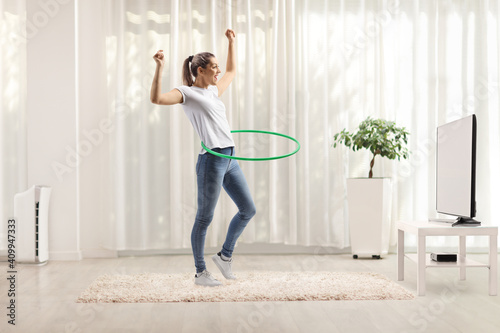 Young woman spinning hula hoop at home in a living room