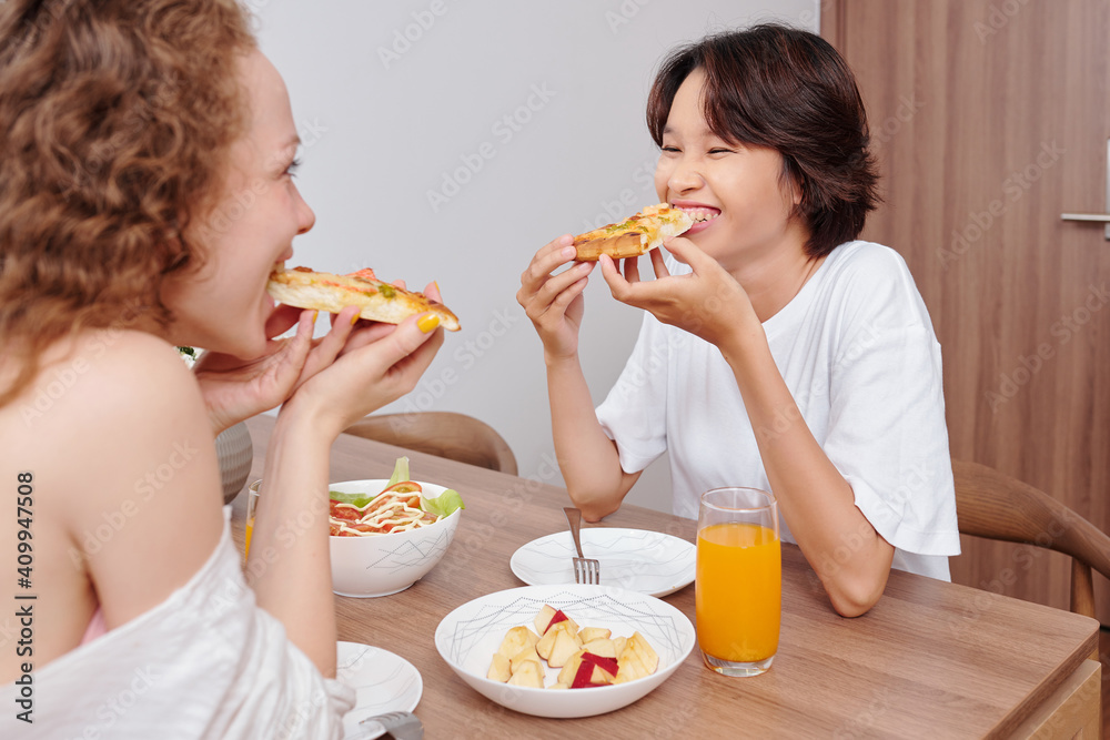 Cheerful hungry young women having delicious pizza, salad and apple slices for dinner Cheerful hungry young women having delicious pizza, salad and apple slices for dinner