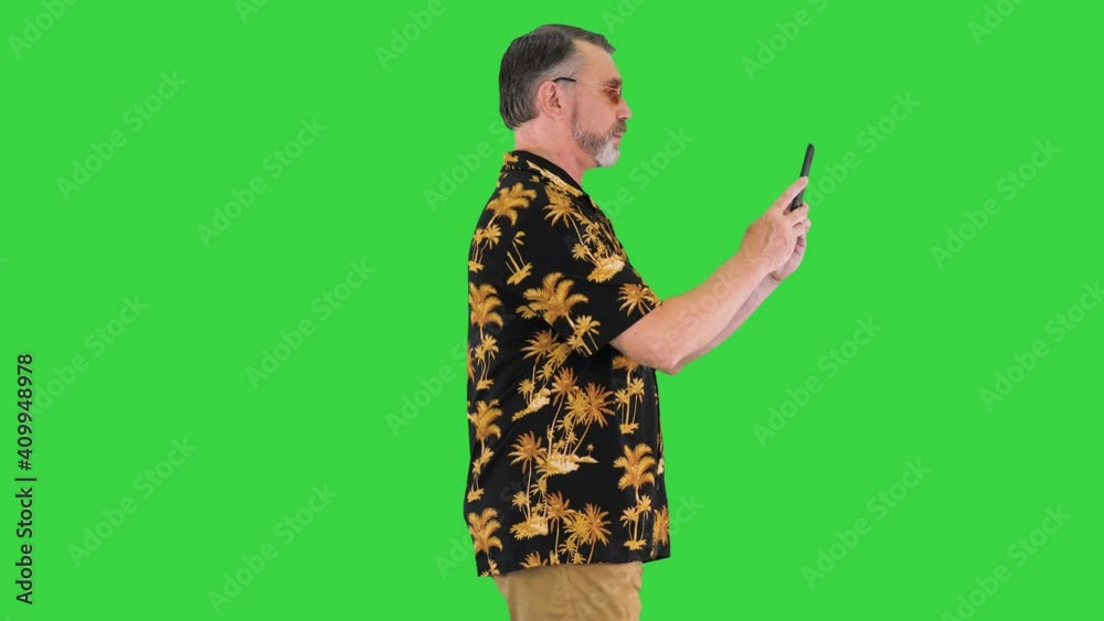 Senior man tourist taking photo by his phone camera while walking on a Green Screen, Chroma Key.