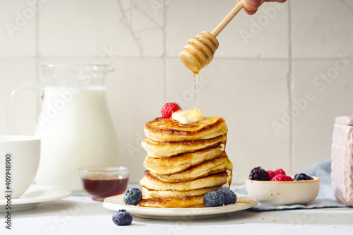 Pouring honey on a stack of fluffy breakfast pancakes with berries and butter photo