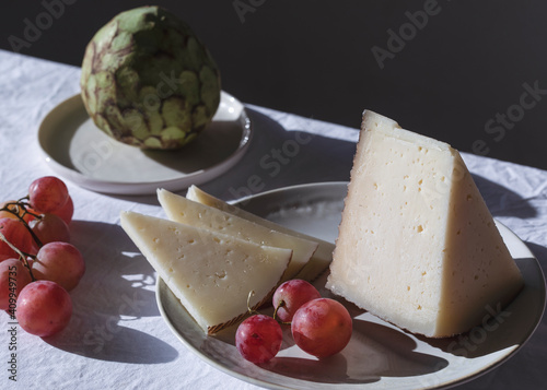 Table with sweet fruits and delectable cheese in bright room lit by sunlight photo