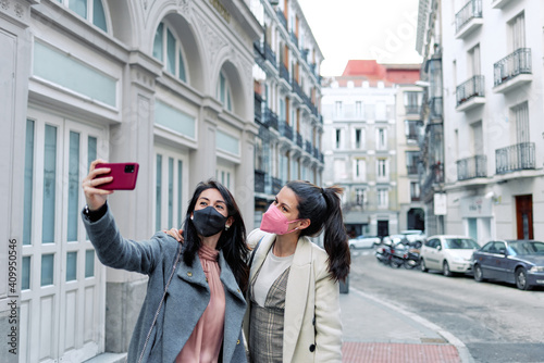 Two women taking a selfie in the street with their face masks on. © David