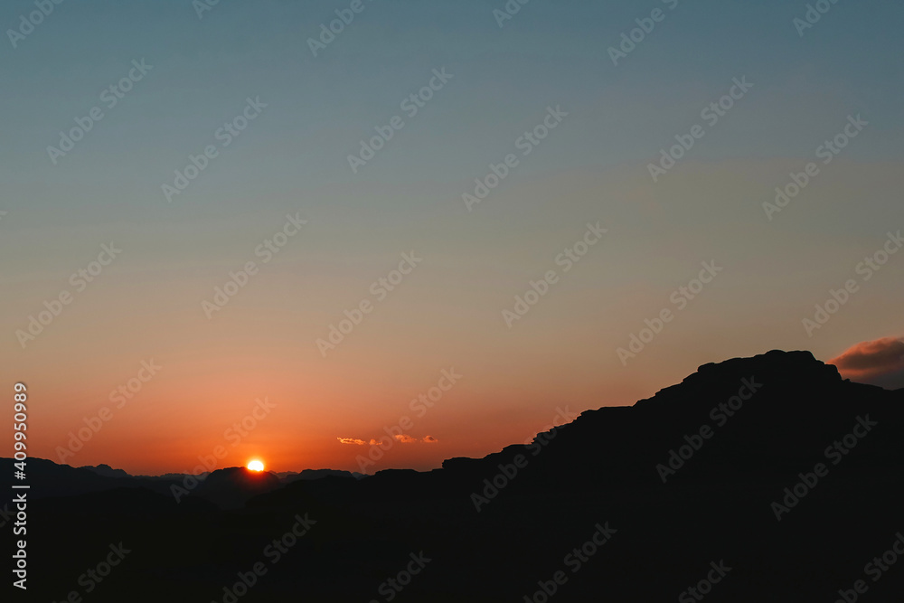 Majestic scenery of orange sunset sun over rocky terrain in Wadi Rum in evening Majestic scenery of orange sunset sun over rocky terrain in Wadi Rum in evening