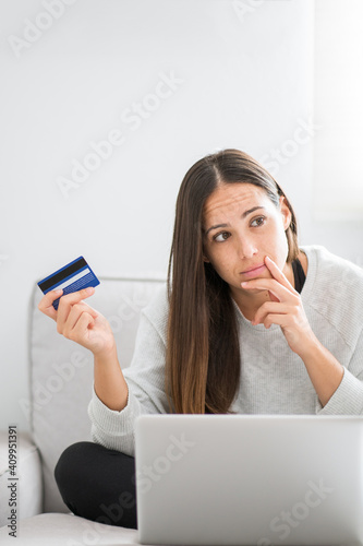 Female buyer sitting on sofa at home and making payment with plastic card while shopping online via laptop