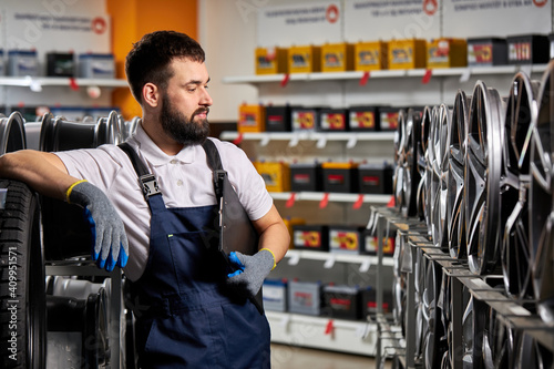 bearded male auto mechanic repairman examining car rims, checking the assortment in his shop, at work place, wearing uniform