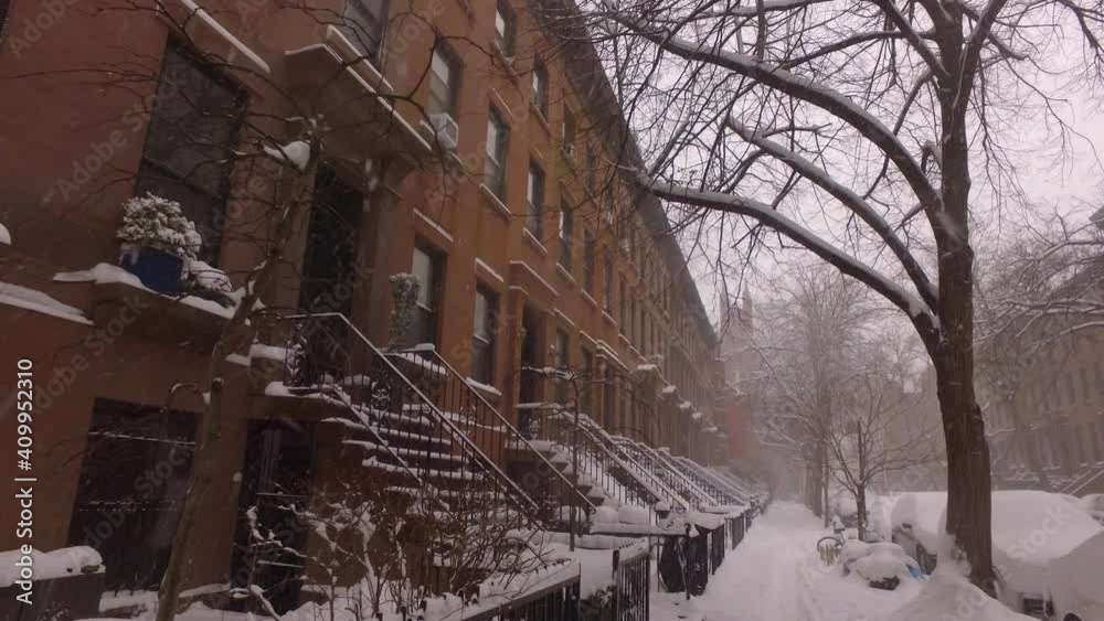 snow falls on a sidewalk along a brownstone block in Brooklyn snow falls on a sidewalk along a brownstone block in Brooklyn
