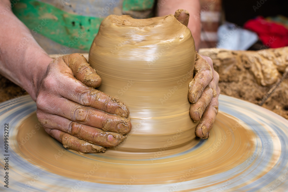 Wet and muddy hands of a craftsman shaping a clay vase on a pottery wheel. Artisan from Ráquira, Colombia. Shallow depth of field