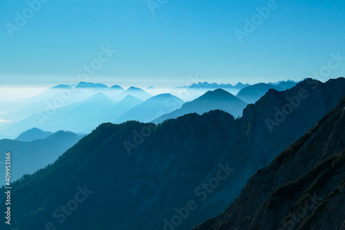 A close up view on the Alpine chains shrouded in the morning fog  seen from the top of Mittagskogel in Austria. Clear and sunny day. Sharp peaks around. Sun is shining above the high peaks. Serenity