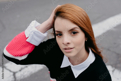 High angle of carefree female with red hair and in casual outfit standing in city street and looking at camera