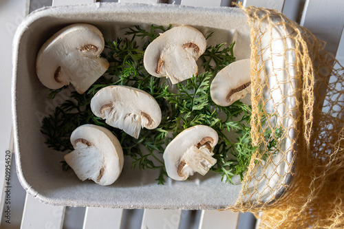 Top view of halved fresh bio organic champignons with green herbs in pot with eco sac placed on white plank surface photo