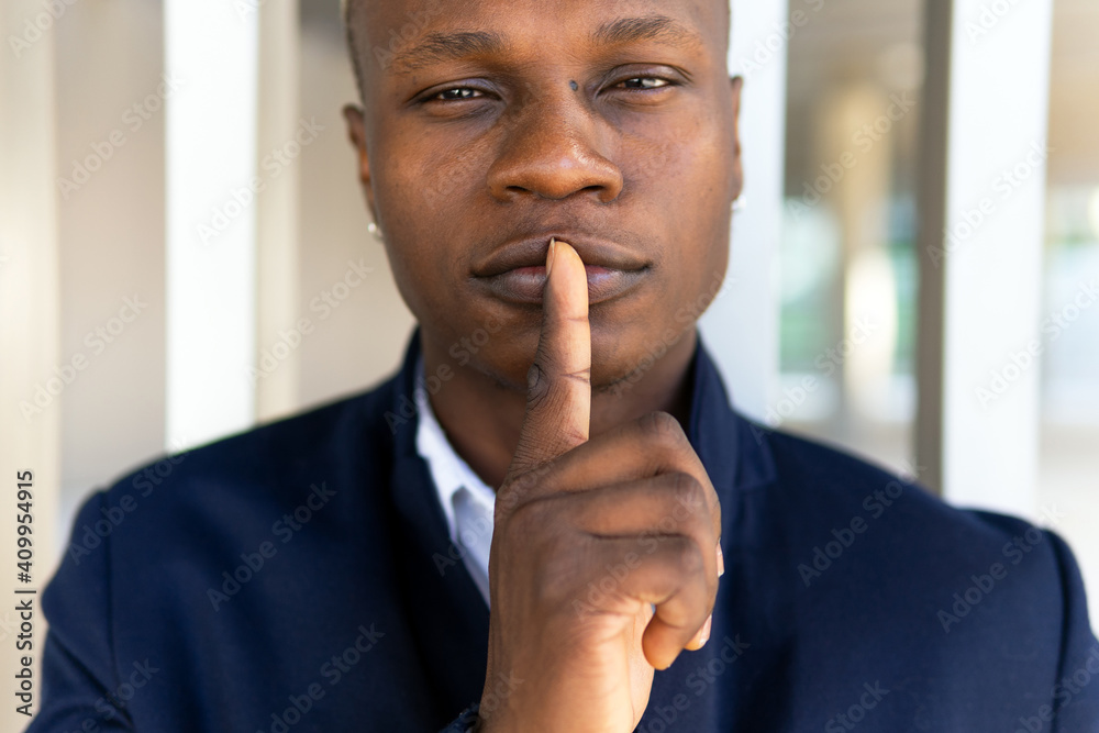 © David Munoz/ADDICTIVE STOCK - Satisfied African American male in casual outfit looking at camera on white background and making silence gesture