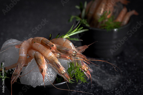 Raw prawns placed in bowl with ice cubes and green herbs on dark table in kitchen of restaurant
