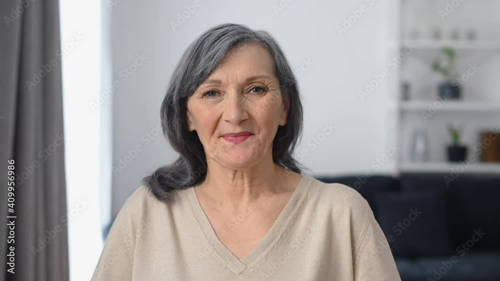 Webcam view of a smiling senior woman waving hello into the camera, older female teacher look at camera conducts online lesson, webinar. Video meeting with a grey-haired grandmother Webcam view of a smiling senior woman waving hello into the camera, older female teacher look at camera conducts online lesson, webinar. Video meeting with a grey-haired grandmother