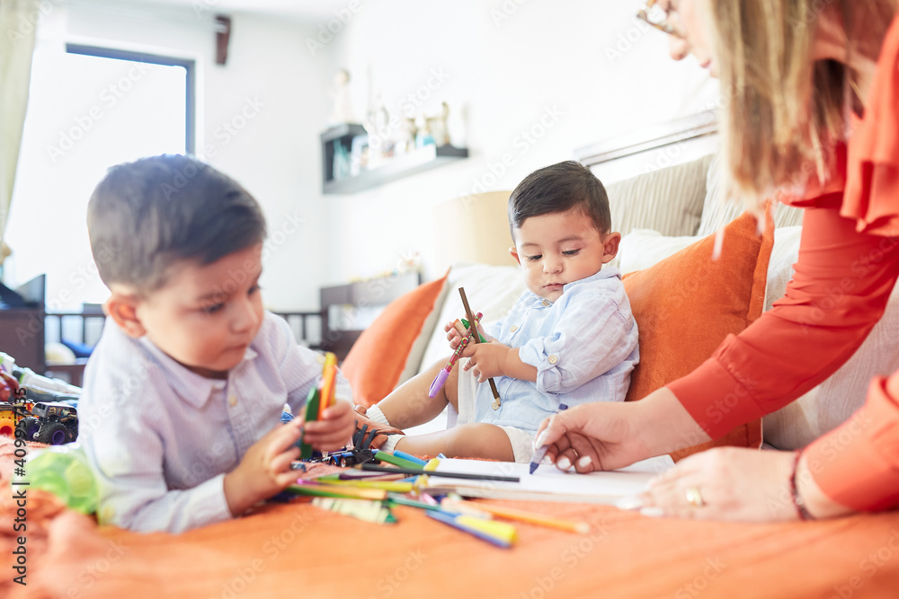 Low angle of mother drawing together with cute little boys while gathering on comfortable bed at home at weekend Low angle of mother drawing together with cute little boys while gathering on comfortable bed at home at weekend