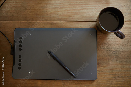 Top view of arrangement of modern graphics tablet with stylus and cup coffee on wooden table photo