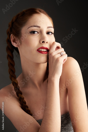 Stylish female model with red hair and braids sitting in studio on dark background and looking at camera