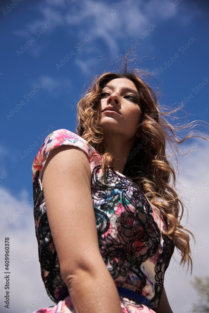 From below of female with long wavy hair and in dress standing on background of blue sky and looking away From below of female with long wavy hair and in dress standing on background of blue sky and looking away