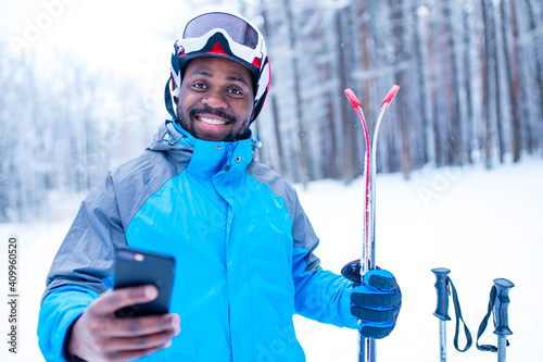 afro american man in blue jacket run ski outdoors in freeze forest holding a phone on hands photo