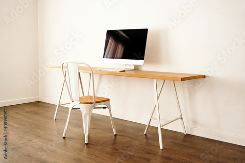 Modern computer placed on wooden table near chair in contemporary light room with minimalist interior