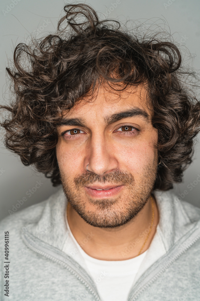 Handsome young unshaven ethnic male with curly hair looking seriously at camera against gray background Handsome young unshaven ethnic male with curly hair looking seriously at camera against gray background