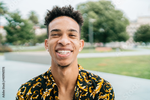 Optimistic African American male in fancy apparel and with Afro hairstyle standing on street and sincerely smiling at camera photo