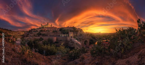 View across river of old city Toledo in Spain with medieval castles and fortresses at sunset time with cloudy sky and reflection in river water