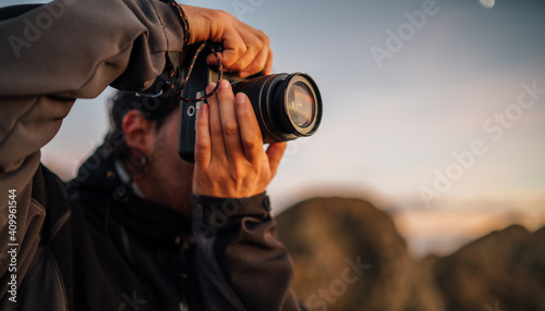 Side view of unrecognizable male photographer with professional photo camera taking pictures of nature while standing on top of rocky mountain photo