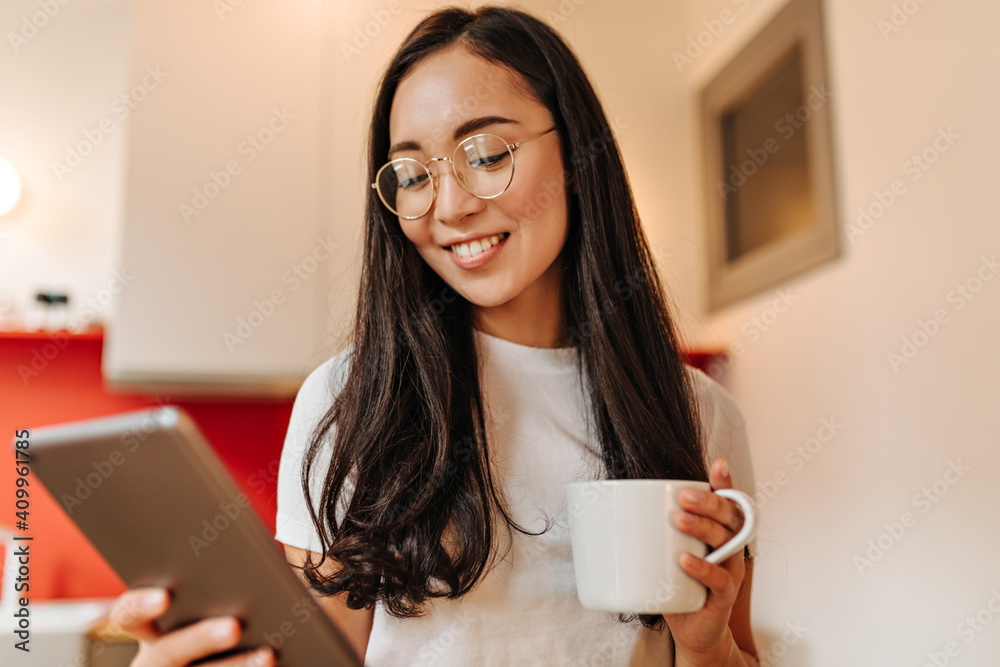 Asian woman with smile reads news in tablet and holds cup of coffee Asian woman with smile reads news in tablet and holds cup of coffee