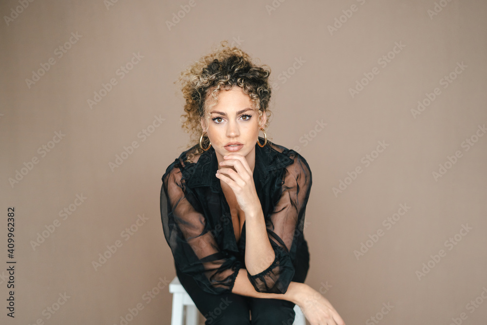 Pensive female in elegant black outfit leaning on hand and looking at camera on brown background Pensive female in elegant black outfit leaning on hand and looking at camera on brown background