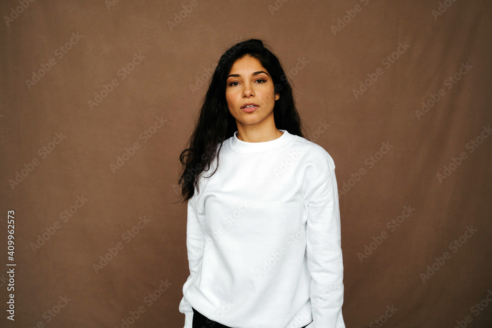 Calm ethnic female in trendy outfit standing on brown background and looking at camera in studio Calm ethnic female in trendy outfit standing on brown background and looking at camera in studio