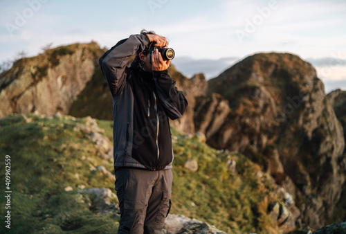 Side view of unrecognizable male photographer with professional photo camera taking pictures of nature while standing on top of rocky mountain photo