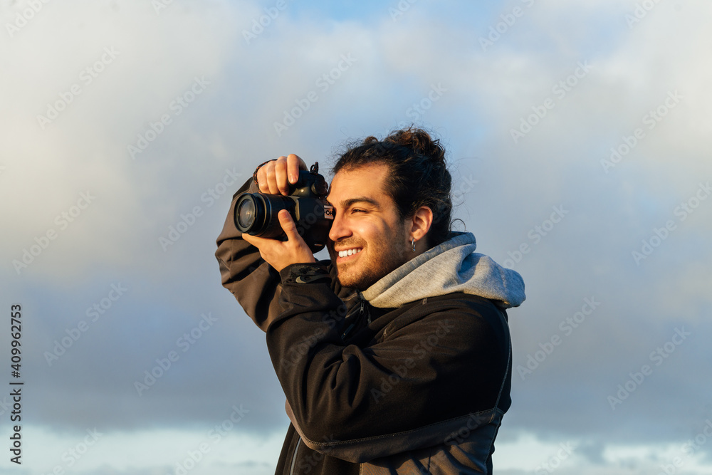 Side view of male photographer with professional photo camera taking pictures of nature while standing on top of rocky mountain Side view of male photographer with professional photo camera taking pictures of nature while standing on top of rocky mountain